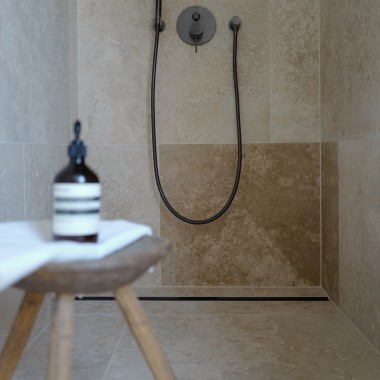 In der sandsteinfarbenen Dusche im Masterbad setzen die schwarzmatten Armaturen und die schwarzmatte CleanLine Duschrinne von Geberit Akzente.