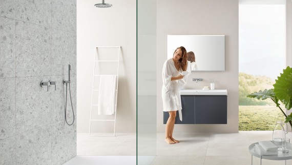 Frau trocknet sich Haare mit Handtuch in Bad mit offener Dusche und grossen Fliesen im Terrazzo-Stil