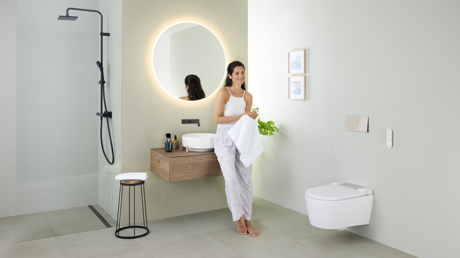 Frau lehnt am Waschtisch an in einem Bad mit Dusch-WC Geberit AquaClean Sela und Waschbecken und Badmöbel Geberit VariForm Frau lehnt am Waschtisch an in einem Bad mit Dusch-WC Geberit AquaClean Sela und Waschbecken und Badmöbel Geberit VariForm
