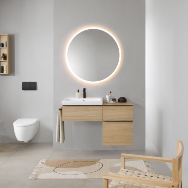 Bad mit grauen Wänden, Geberit Badmöbeln aus Holz und einem runden Geberit Option Lichtspiegel