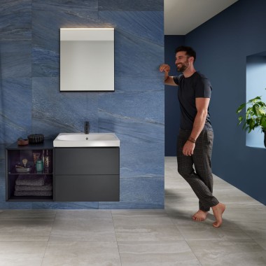 Mann lehnt an Wand in blauem Badezimmer mit Geberit Mix & Match Waschplatz Mann lehnt an Wand in blauem Badezimmer mit Geberit Mix & Match Waschplatz