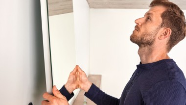 Mann hängt während Badrenovierung Geberit Option Spiegel auf (c) Geberit
